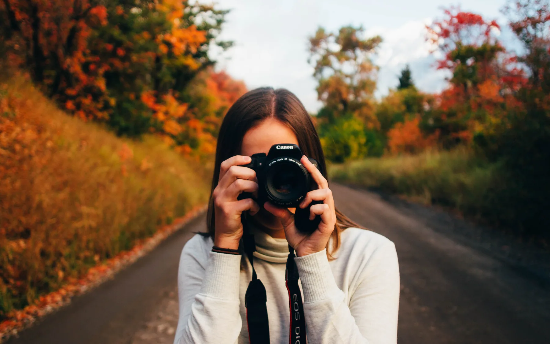 A photographer raising a camera on a tree-lined road in autumn
